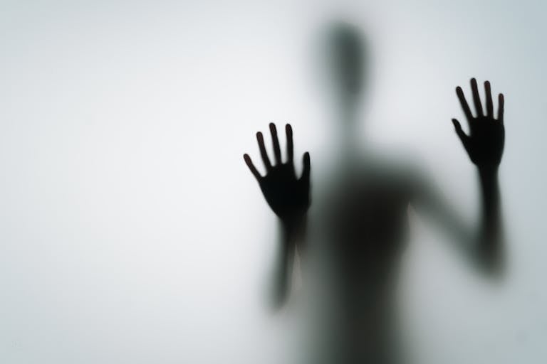 Abstract silhouette of person with hands against glass, creating a mysterious vibe.